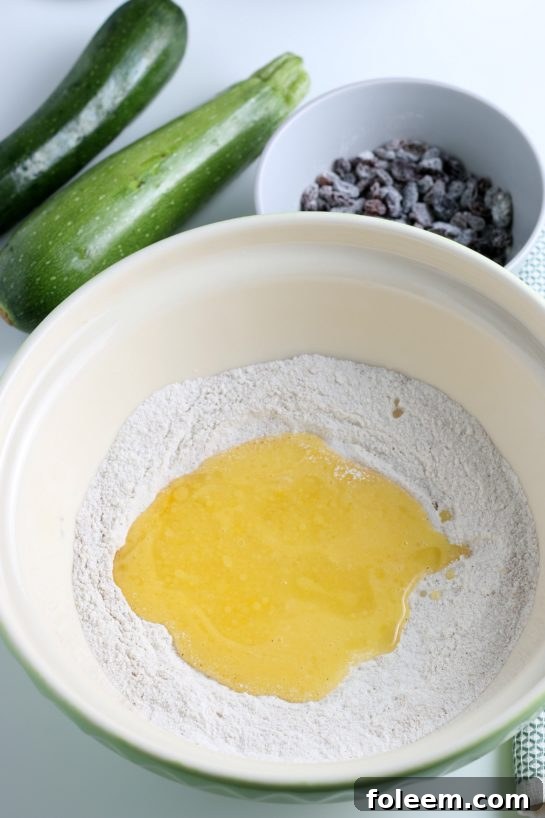 Whisked eggs and oil being poured into the bowl of dry ingredients, signaling the next step in combining the wet and dry components for the zucchini muffins.