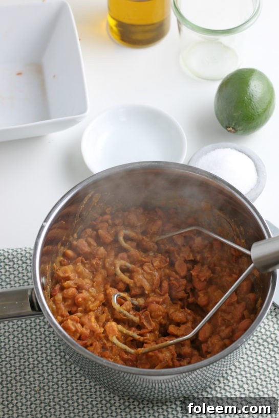 Mashing the cooked pinto beans in the pot with a potato masher for perfect refried beans.