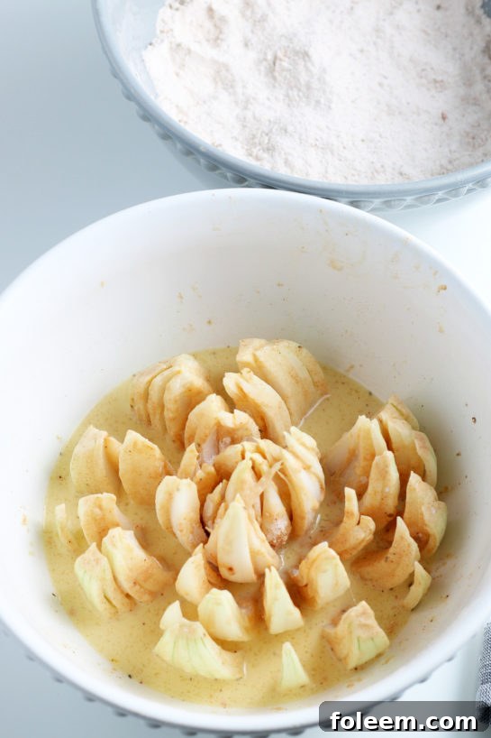 A close-up shot of the meticulously cut onion being immersed in the rich, spiced batter before frying, showing the detailed coating.