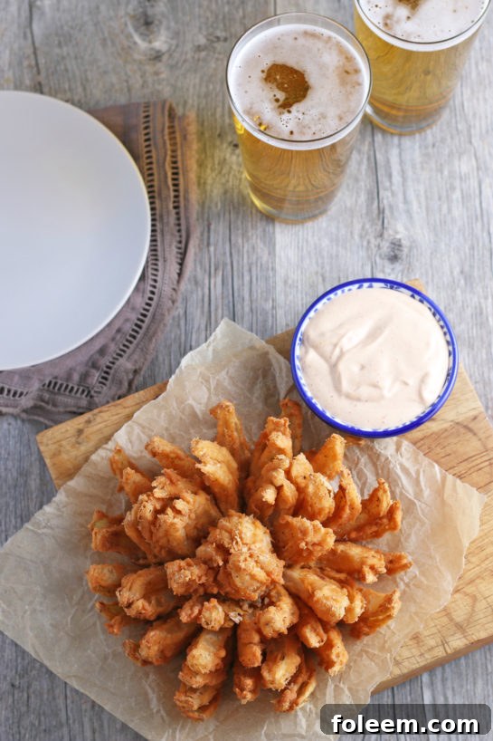 Overhead view of a perfectly fried blooming onion, golden brown and served with a ramekin of homemade dipping sauce, ready to be enjoyed.