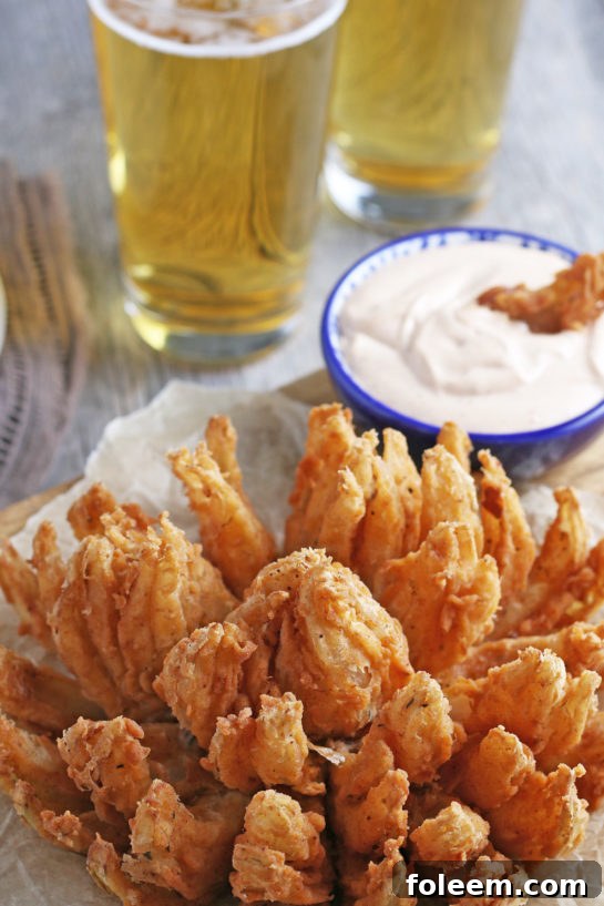 Deep-fried blooming onion showcasing its beautiful 'bloom' effect and golden crispiness, served alongside its creamy dipping sauce.