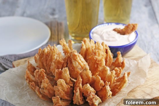 Close-up of a blooming onion petal dipped in a savory homemade sauce, highlighting the crispy texture and delicious flavor.