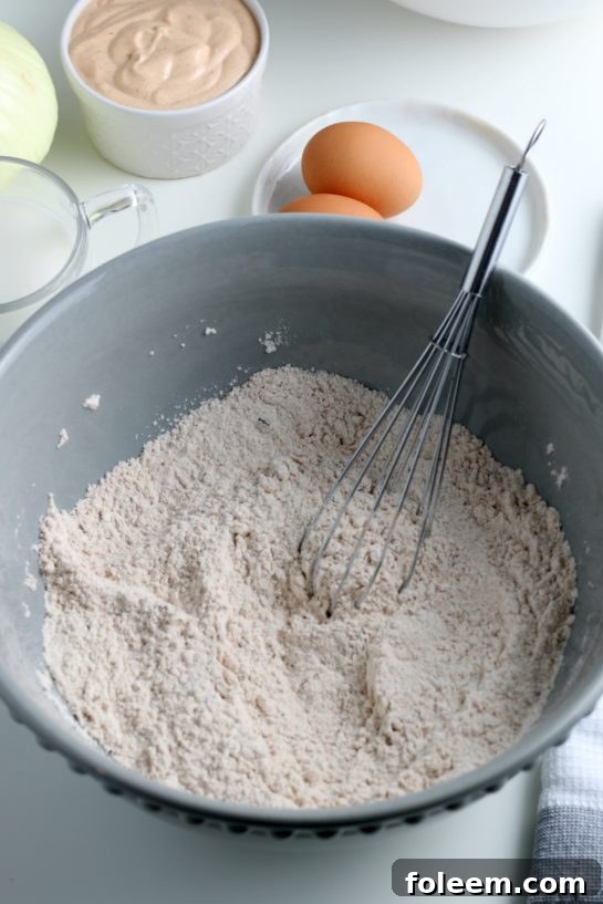 A close-up of dry ingredients and spices being thoroughly mixed in a bowl, forming the base for the crispy blooming onion coating.