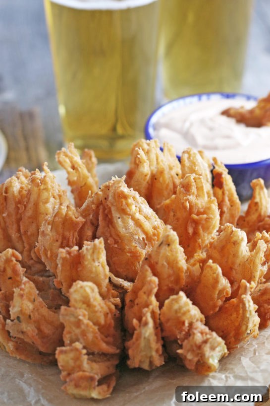 A beautifully fried blooming onion, golden and crispy, served with a creamy homemade dipping sauce on a dark background.