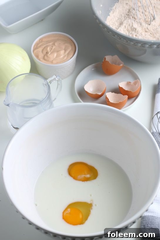 Two large eggs being cracked into a bowl of dry ingredients, preparing the wet batter for the blooming onion recipe.