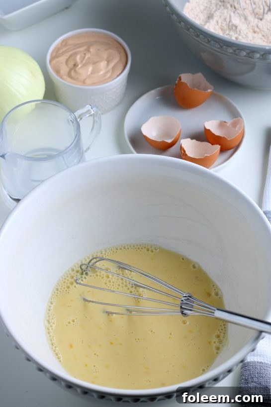Wet ingredients, including eggs and milk, being whisked together in a bowl to create a smooth, consistent batter for frying.