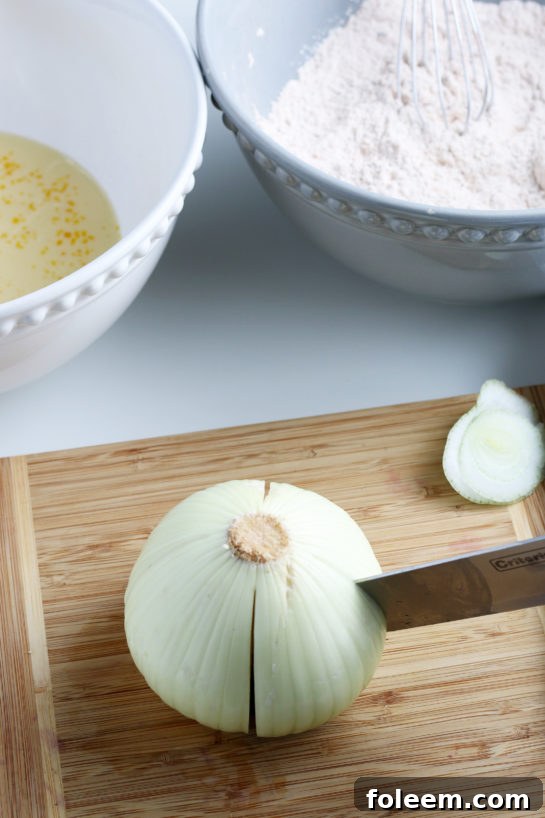 A sweet onion being carefully sliced with a knife on a cutting board, preparing it for the blooming onion recipe.