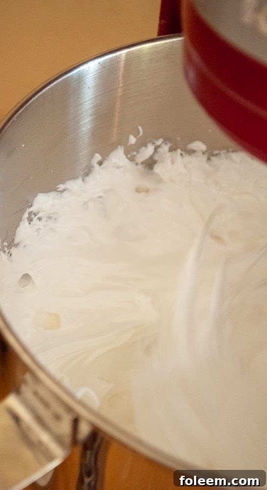 A stand mixer vigorously whipping egg whites and other ingredients to create fluffy meringue for Halloween Boo Meringues.