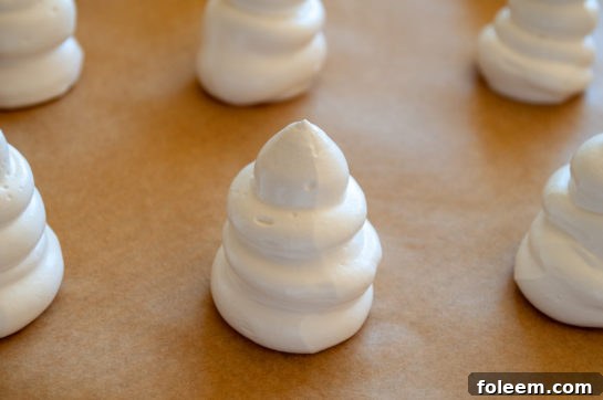 Meringue being piped onto a baking sheet, forming the characteristic ghost shapes for Halloween Boo Meringues.