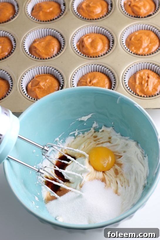 A bowl of pumpkin muffin batter being thoroughly mixed with eggs and other wet ingredients to create a smooth, unified consistency for Simple Pumpkin Cream Cheese Muffins.
