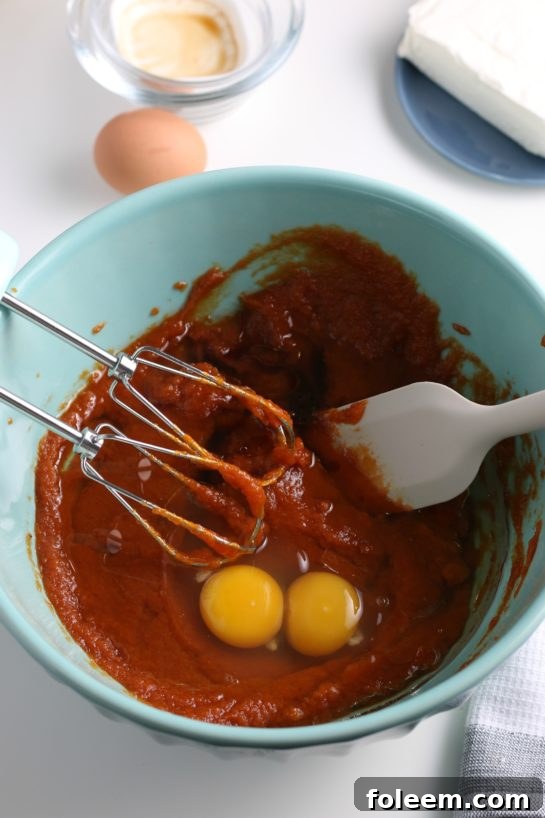 Cracking eggs into the pumpkin mixture, an essential step for binding and enriching the pumpkin cream cheese muffin batter.