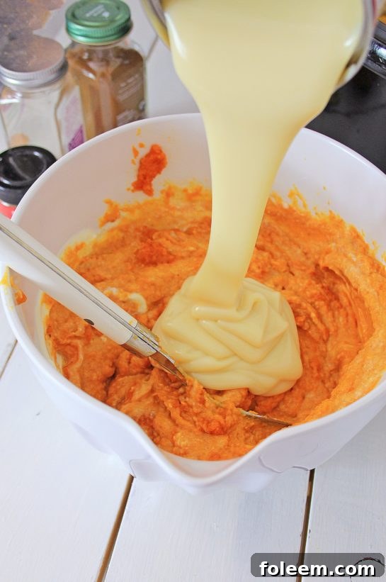 Pouring sweet condensed milk into the pumpkin mixture for a creamy slow cooker bread pudding custard.