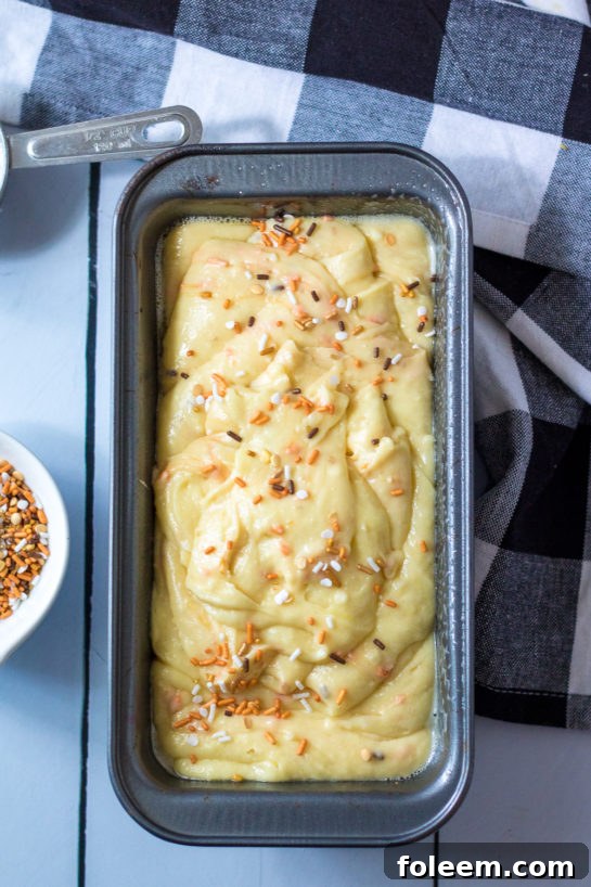 Pouring the colorful batter into a bread loaf pan, ready for baking this delightful Fall Confetti Sweet Bread.