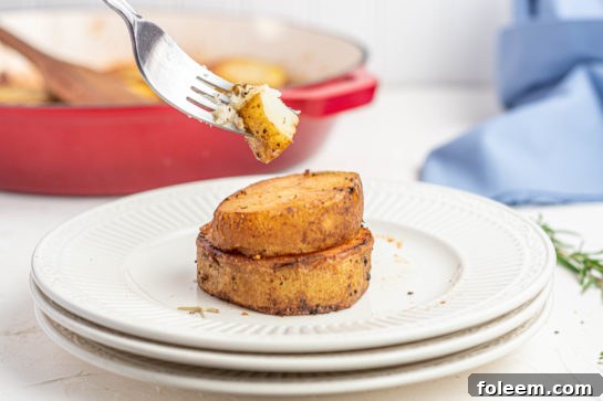 Top-down view of a large platter of melting potatoes, garnished with fresh rosemary