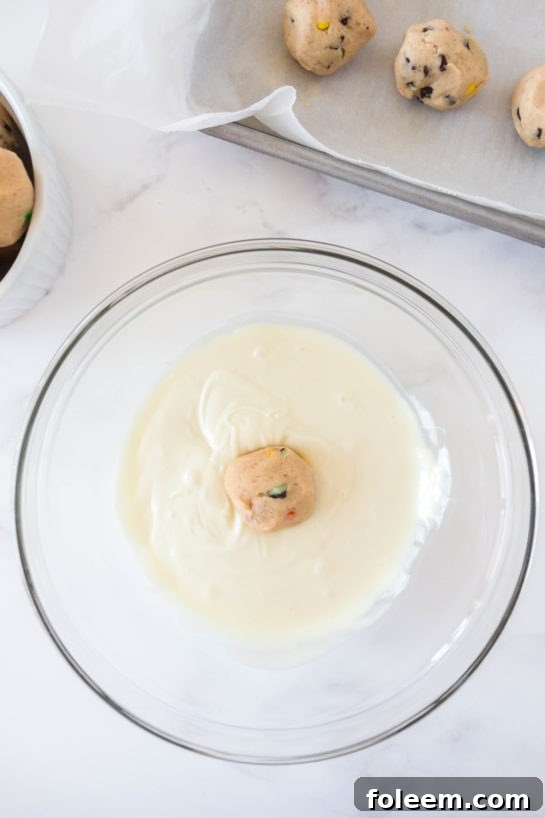Dipping the dough balls in the white chocolate for Edible Cookie Dough Bombs recipe