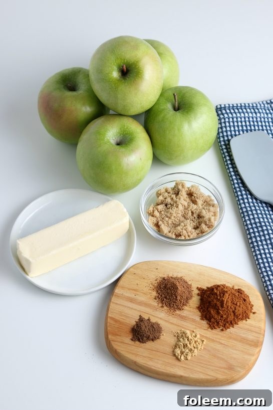 Assortment of fresh ingredients laid out on a wooden board, including apples, butter, cinnamon, nutmeg, and brown sugar, ready for making fried apples.