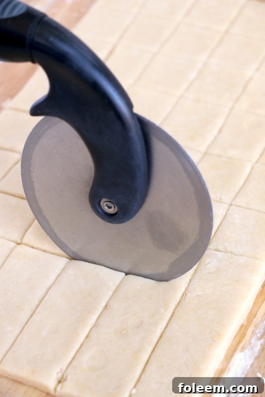Precisely slicing the rolled-out dough into small squares using a pizza cutter for the cookie bites.