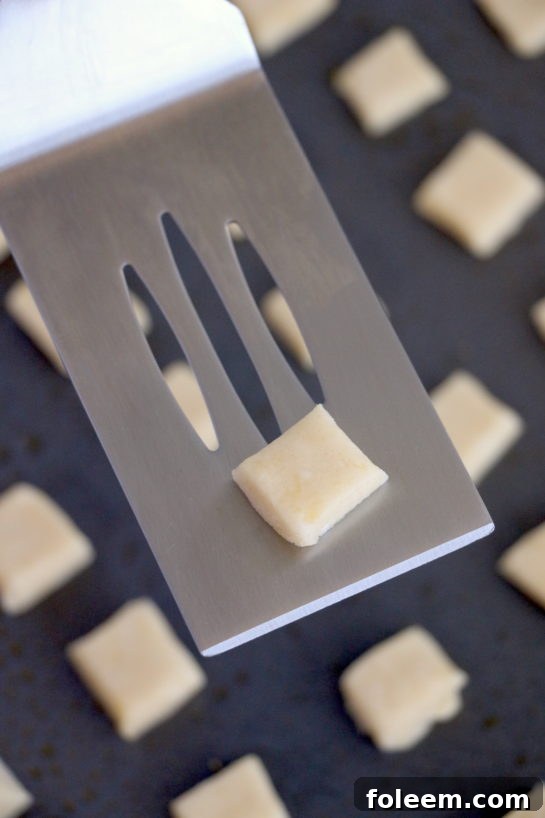 Carefully placing the small dough squares onto a greased baking sheet before baking.