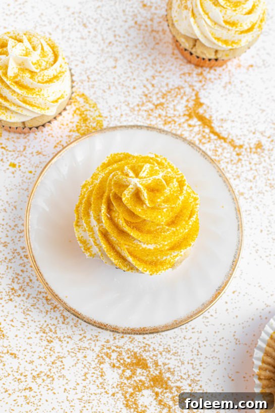 Overhead shot displaying multiple frosted Champagne Cupcakes adorned with sparkling gold sprinkles, arranged for a festive display.