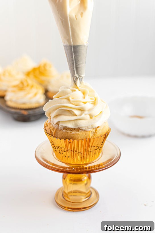 A skilled hand piping luscious champagne buttercream frosting onto a freshly baked Champagne Cupcake, creating an artistic swirl.