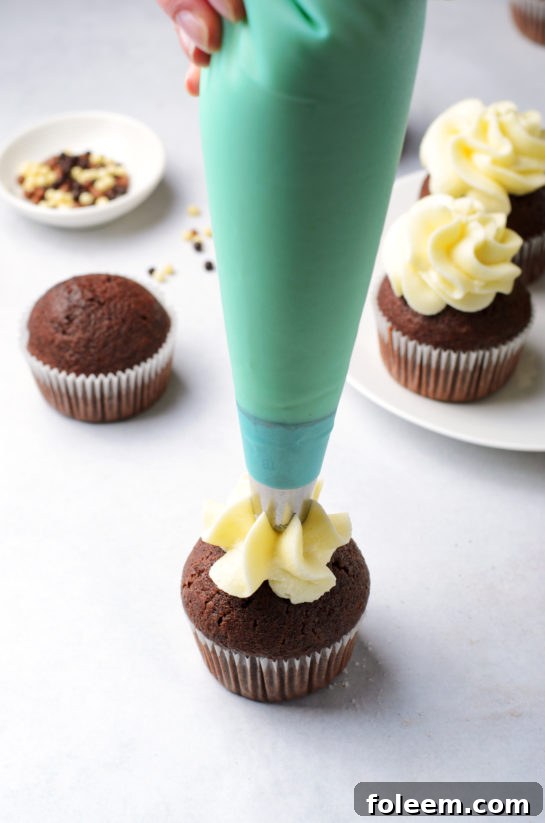 Expertly piping creamy frosting onto the delicate chocolate cupcakes.