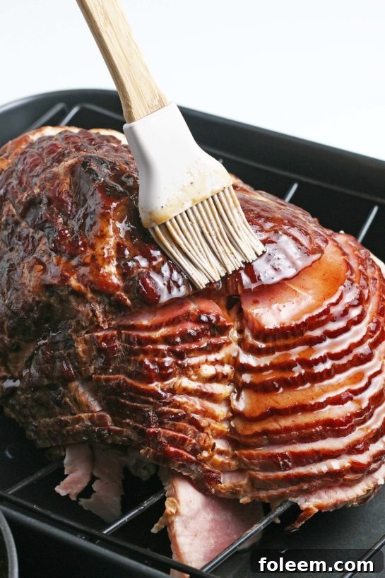 Chef brushing a vibrant, rich glaze onto a spiral ham, ensuring every slice is coated with sweet and savory flavor before baking.