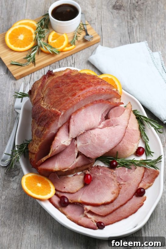 An overhead view of the whole spiral ham, resting in a roasting pan, glistening with the initial layer of sweet glaze.