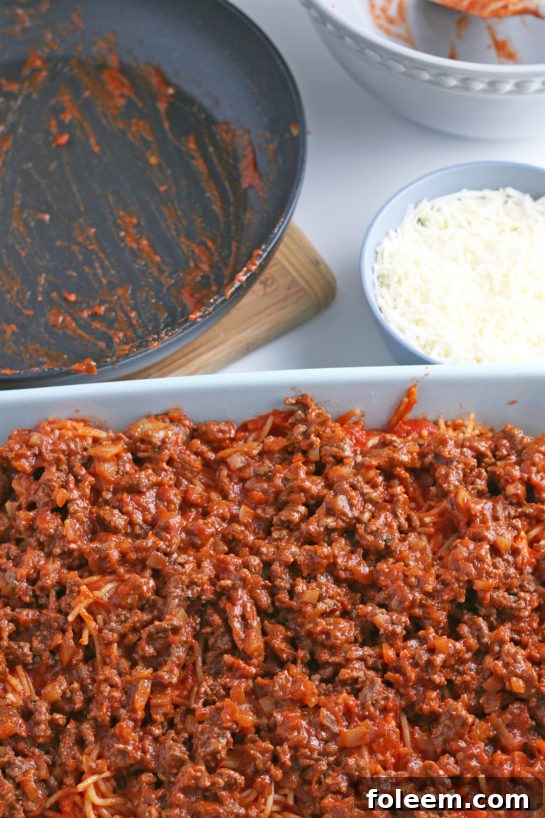 A hearty layer of savory meat sauce is spread over the spaghetti and cream cheese, preparing the casserole for its final cheese topping.