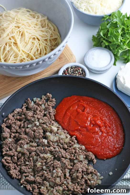 The cooking process begins with browned ground beef and diced onions simmering in a rich tomato sauce, forming the flavorful base.