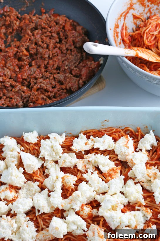 A generous layer of creamy cheese is spread over the first layer of spaghetti and sauce, adding richness and flavor.