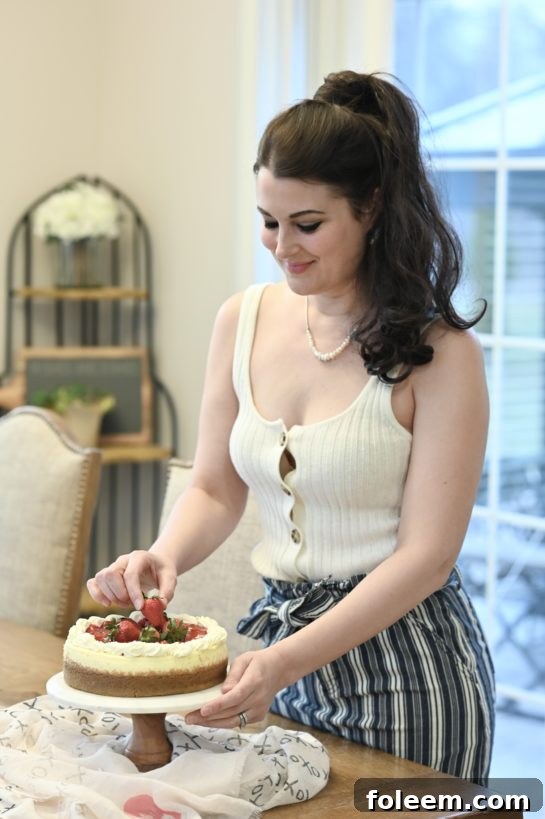 Fresh strawberries being arranged artistically atop a finished New York-Style Cheesecake, highlighting the topping process