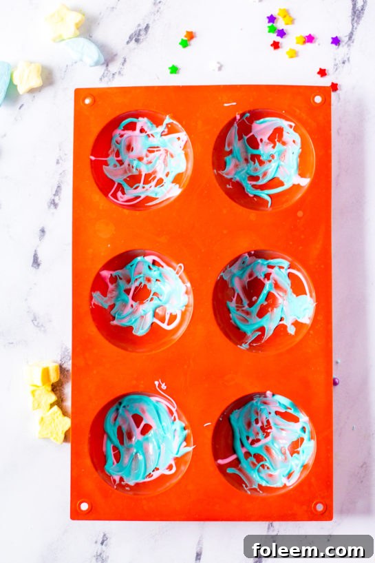 Silicone molds with blue and pink melted chocolate for Galaxy Hot Chocolate Bombs.