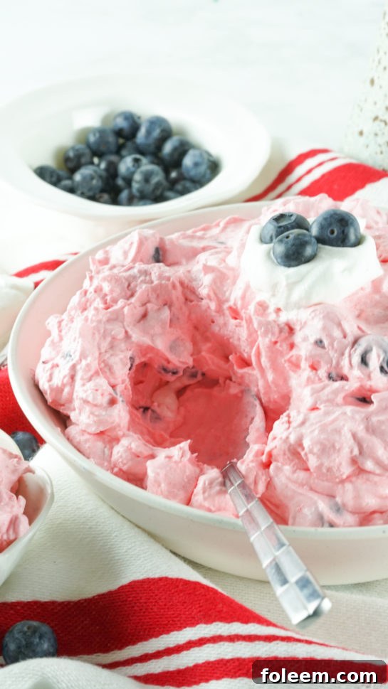 A hand scooping the creamy Red White and Blue Fluff Salad into a serving dish.