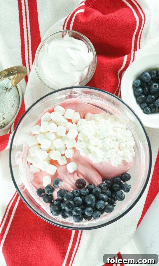 Adding fresh blueberries and mini marshmallows into the mixed ingredients for the Red White and Blue Fluff Salad.