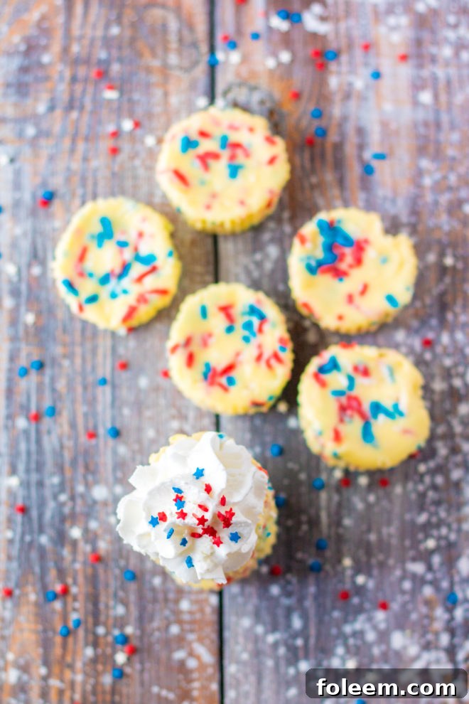 Red, White, and Blue Mini Cheesecakes recipe layered with a Golden Oreo crust and creamy tangy cheesecake. Top with sprinkles and whipped cream for the perfect patriotic dessert for Memorial Day or 4th of July!