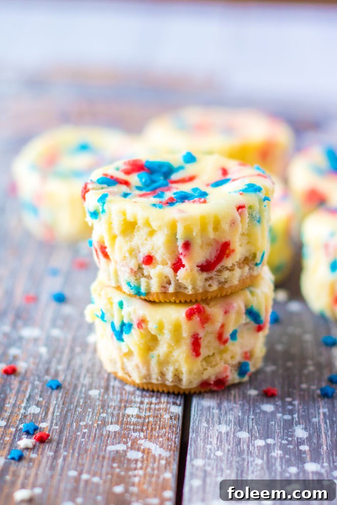 Easy Mini Red, White, and Blue Cheesecakes recipe layered with a Golden Oreo crust and creamy tangy cheesecake. Top with sprinkles and whipped cream for the perfect patriotic dessert for 4th of July!