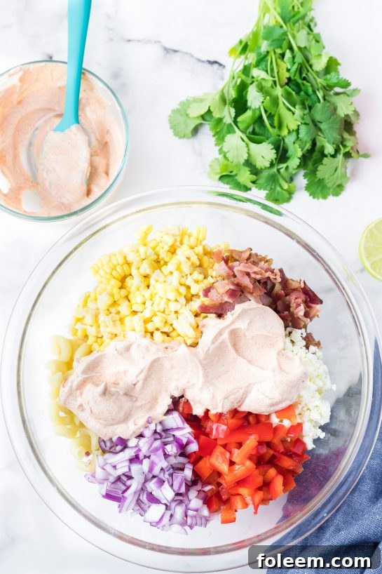 Pouring the rich dressing over the dry ingredients for Mexican Street Corn Pasta Salad.