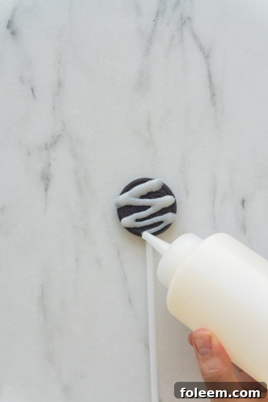 Piping the white glaze onto an Oreo cookie to create the mummy effect.