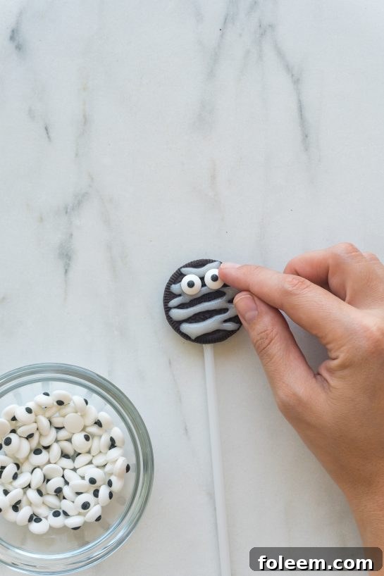 Placing candy eyes on a Mummy Oreo Pop before the glaze sets.