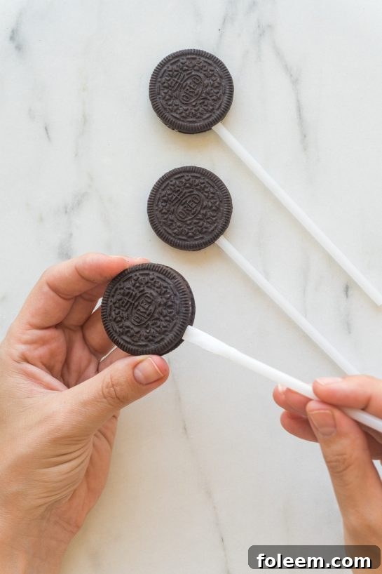 Inserting lollipop sticks into Oreo cookies to create the base for Mummy Oreo Pops.