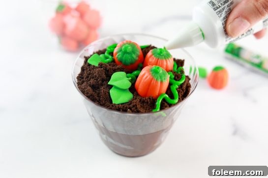 Close-up of finished Pumpkin Patch Dirt Cups showcasing candy pumpkins and green icing vines