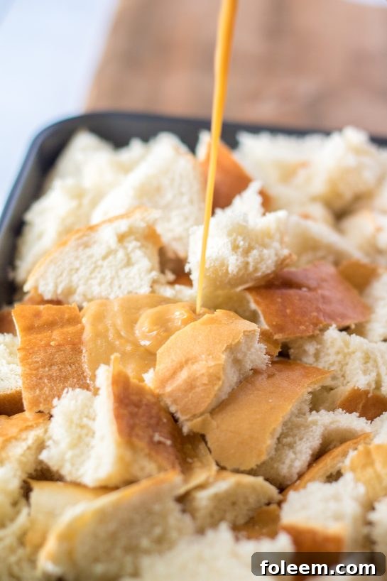 A stream of creamy, spiced sweet potato and egg mixture being poured evenly over the cubed bread in a baking dish, ensuring every piece is well coated.