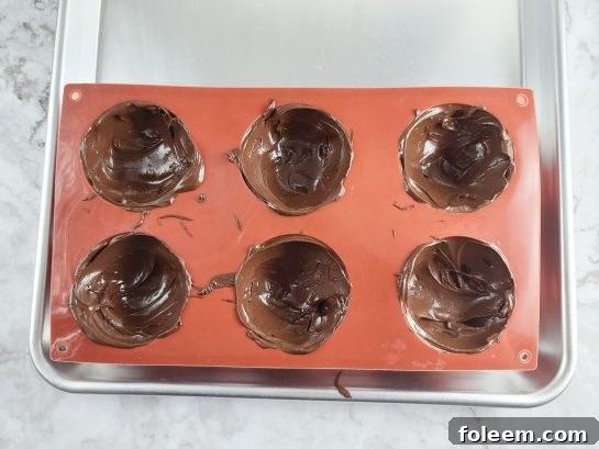 Pouring melted chocolate into silicone molds to form half-spheres for Hot Chocolate Bombs.