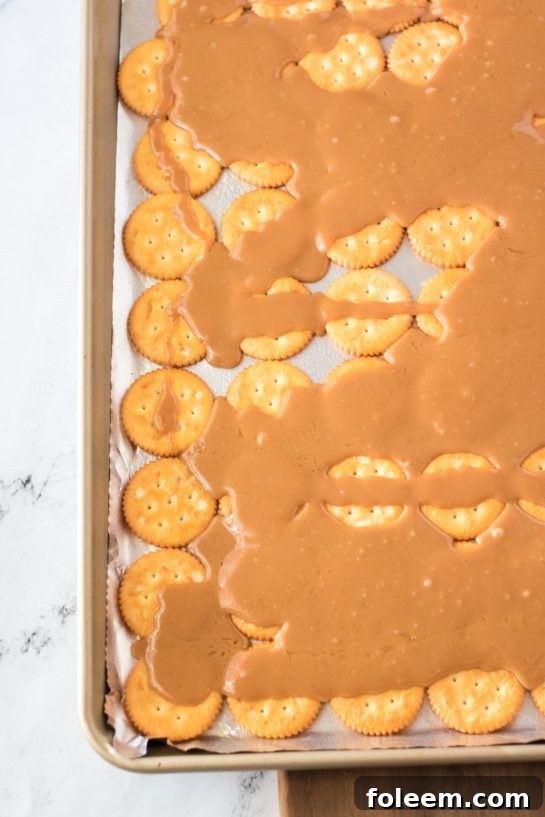 Hot stovetop toffee being carefully poured over a layer of Ritz crackers in a baking pan.