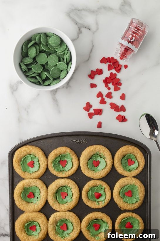 Melted green chocolate filling the cookie cups, ready for heart sprinkles.