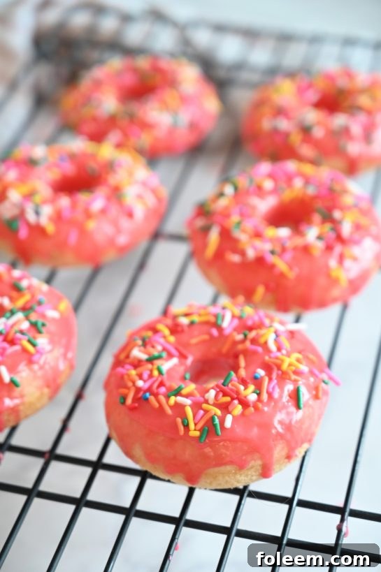 Close-up of a stack of vanilla-glazed baked donuts with festive pink frosting and sprinkles, highlighting the soft cakey texture. These are ideal for breakfast, brunch, or a sweet dessert.