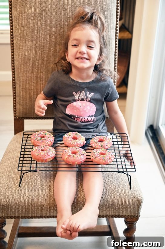 My daughter, Eliza, proudly holding a plate of the freshly made Vanilla-Glazed Baked Donuts, showcasing the joy of homemade treats and family bonding.