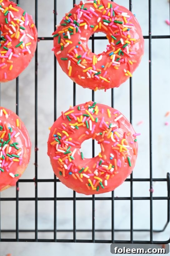 A beautifully arranged plate of vanilla-glazed baked donuts, some with pink glaze, others with classic white, all adorned with colorful sprinkles. Perfect for breakfast or a dessert setting.