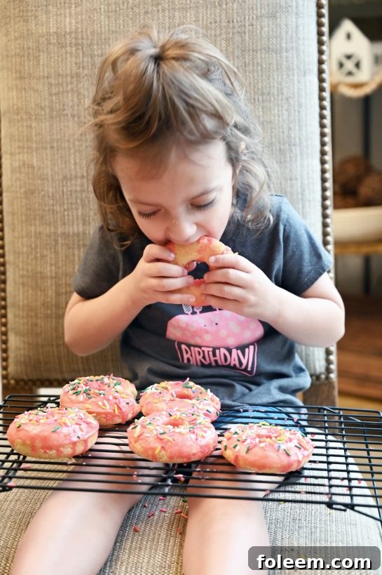 My daughter, Eliza, happily taking a satisfying bite out of a vanilla-glazed baked donut, a testament to its deliciousness and the joy of homemade treats.