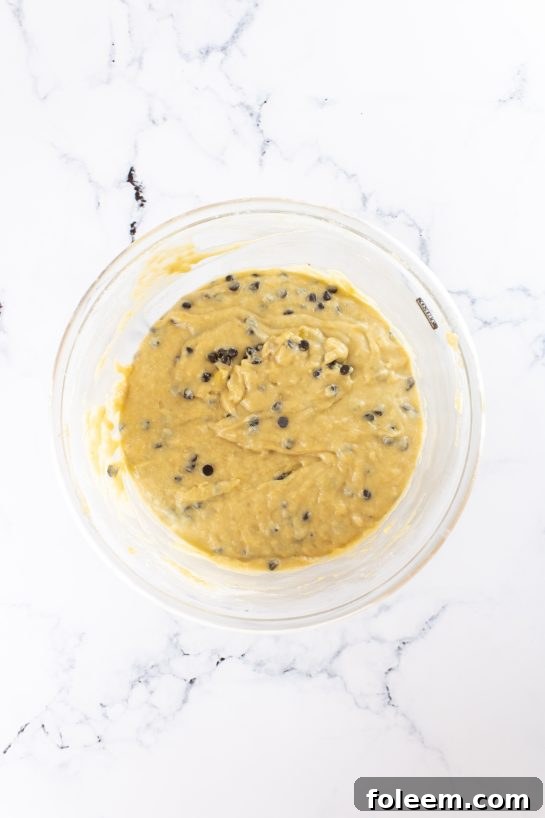 Hands mixing wet ingredients in a bowl for banana chocolate chip muffins.
